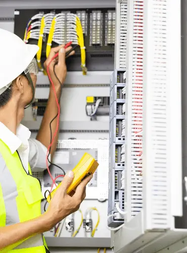 Un elettricista professionista in abiti da lavoro che esegue un controllo di sicurezza e una diagnosi con un multimetro su un quadro elettrico.