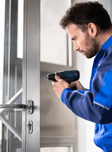 Fabbro professionista che installa o ripara una serratura su una porta utilizzando un avvitatore elettrico, servizio di assistenza a Roma.
