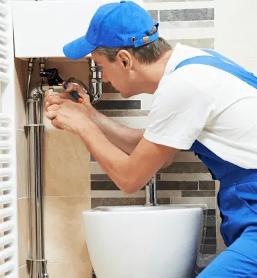 Primo piano di un idraulico specializzato che esegue la manutenzione di precisione sulle tubature di un sanitario per garantire il corretto funzionamento