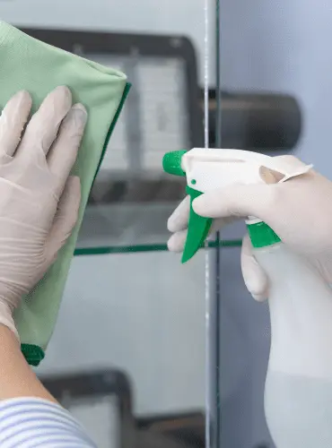 Primo piano di un operatore che esegue la pulizia professionale di una vetrata con panno e spray, garantendo un risultato senza aloni per uffici e negozi a Roma.